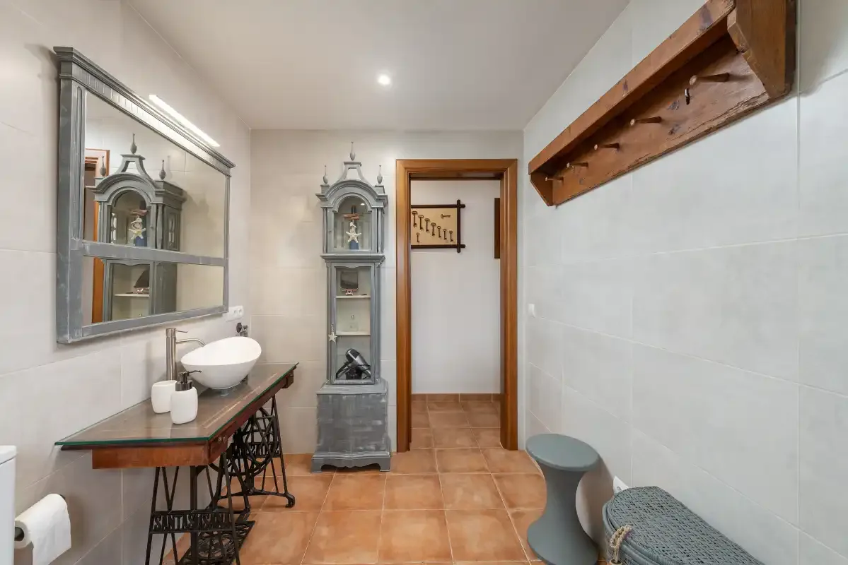Un baño con lavabo sobre encimera, espejo de pared y suelo de baldosas.