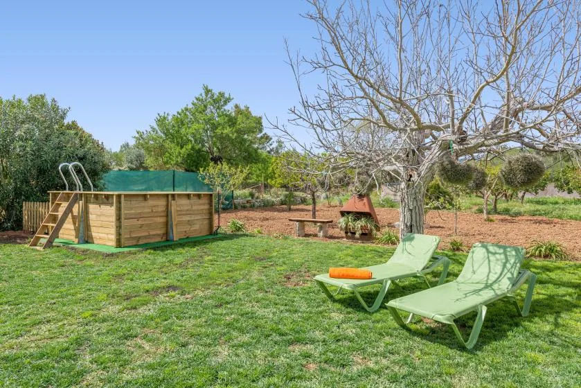 Una zona exterior con césped tiene asientos reclinables junto a una piscina elevada de madera.