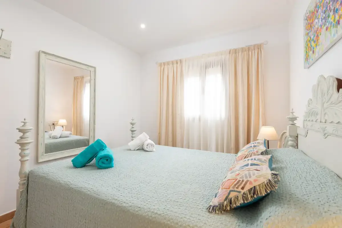 Un dormitorio luminoso con una cama grande y cortinas claras.