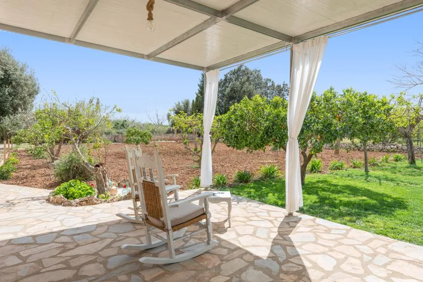 Un patio cubierto con asientos da a un jardín verde y árboles.