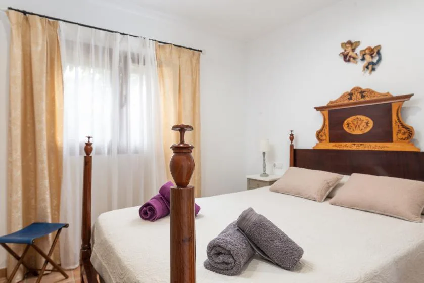 Un dormitorio con una cama grande, ropa de cama clara y una ventana con cortinas.