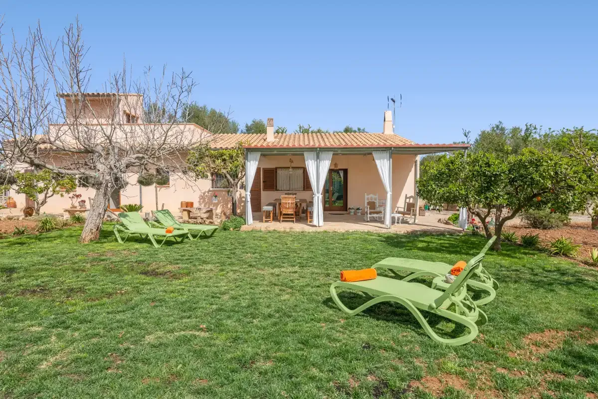 Una casa da a un jardín de césped con asientos verdes para descansar.