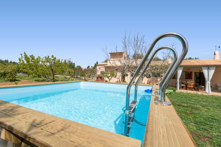Una piscina al aire libre junto a una terraza de madera y un patio cubierto.