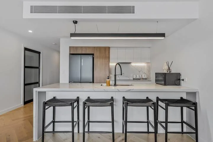 A modern kitchen with a white island and black bar seating.