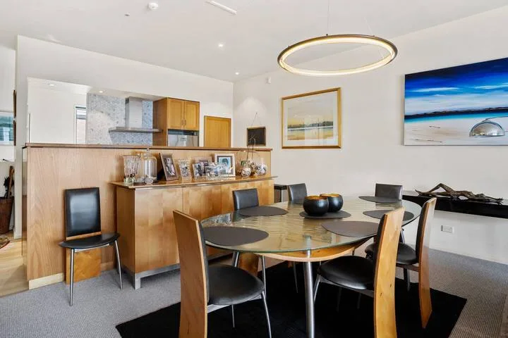 A dining area with a glass table, chairs, and framed coastal artwork.