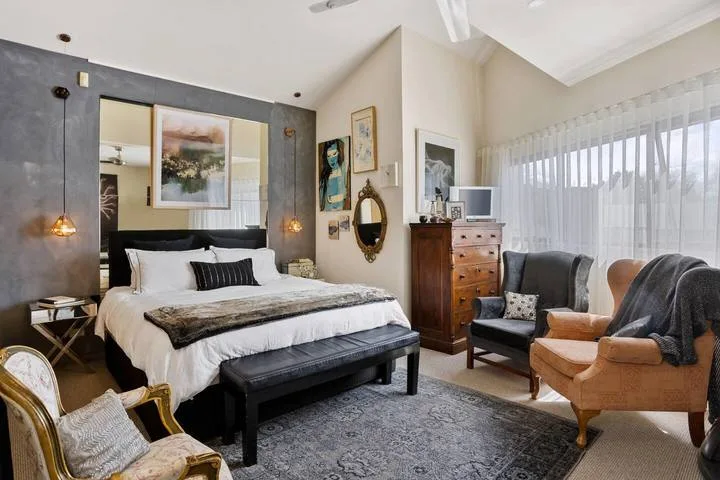 A bedroom with a neatly made bed, seating, and large curtained windows.