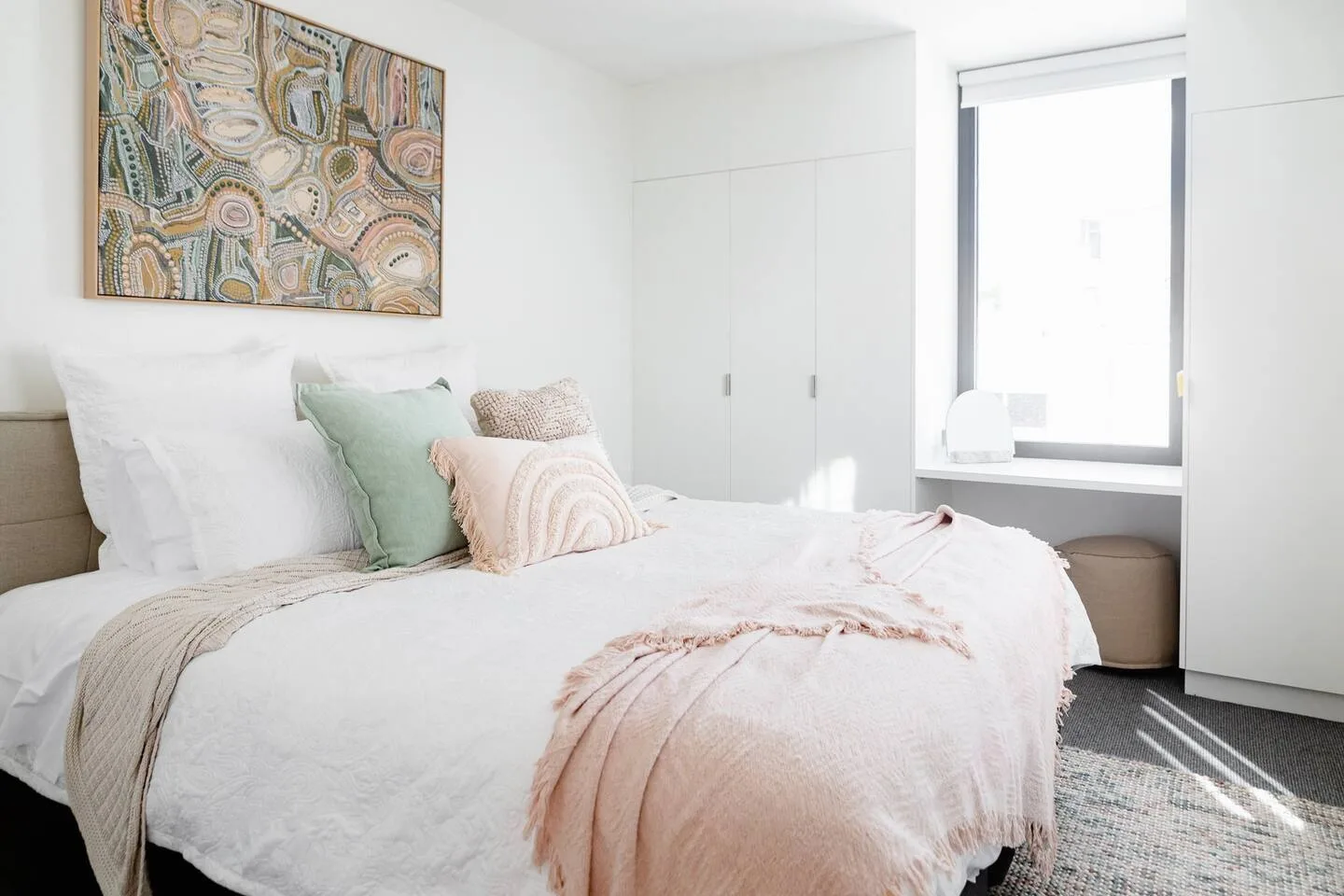 A bright bedroom with a neatly made bed and a large window.