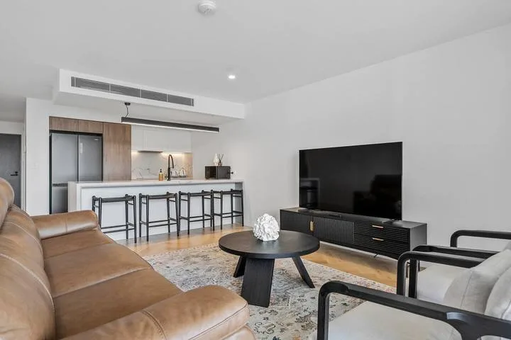 A modern living room with seating, a television, and a kitchen counter.