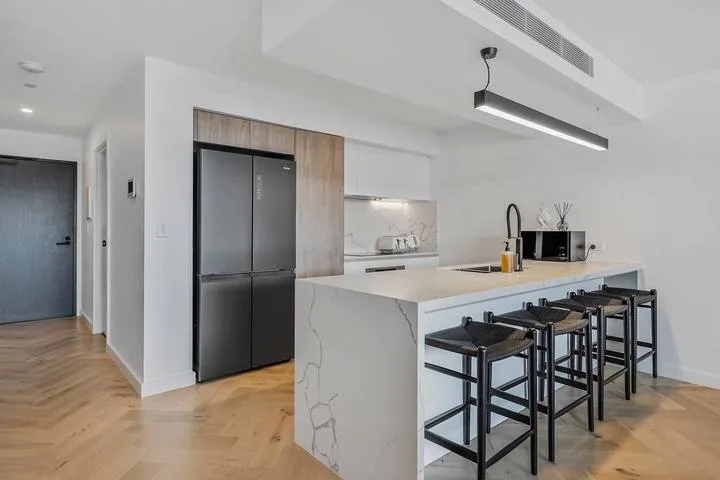 A modern kitchen with a large island, bar seating, and a dark refrigerator.