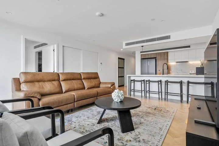 A living room with a brown sofa, coffee table, and open kitchen.
