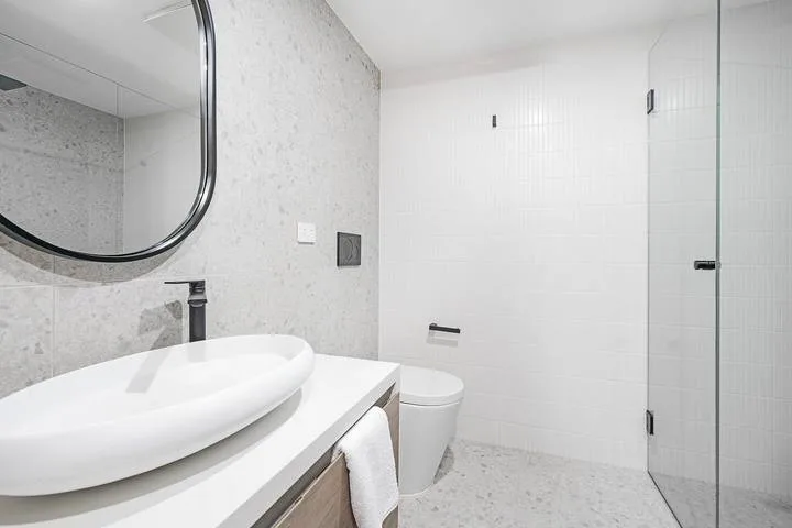 A bright bathroom with a white vessel sink, toilet, and glass shower screen.