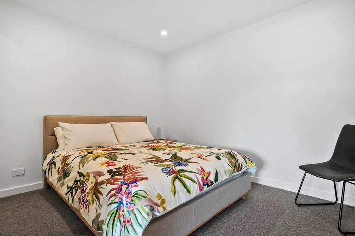 A bedroom with a bed covered in colorful floral bedding and a chair nearby.