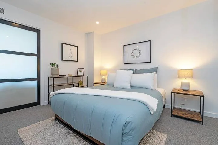 A bedroom with a bed, bedside tables, and framed wall art.