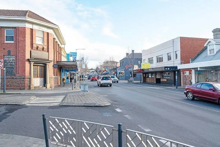 A downtown street with storefronts, parked cars, and a pedestrian crossing.