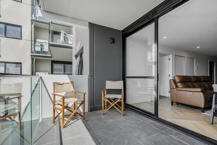 A modern balcony seating area overlooks an adjacent building through glass panels.