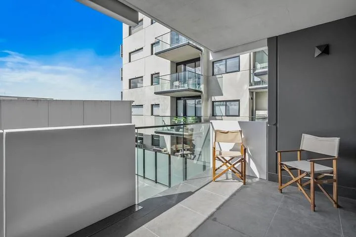 A modern balcony with glass railings and two folding chairs overlooks a neighboring building.