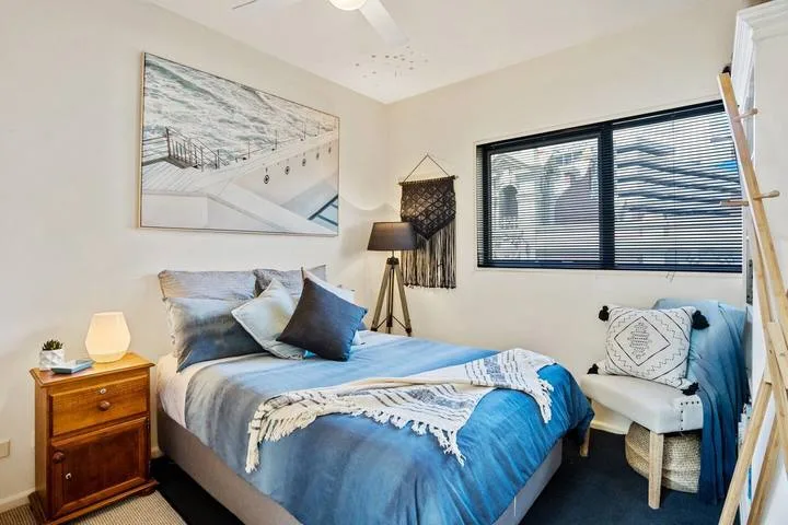 A bedroom with a bed dressed in blue bedding and a window with blinds.