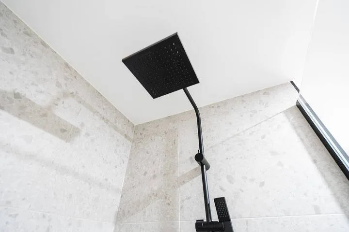 A shower with a square overhead showerhead against light stone-patterned walls.
