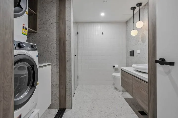 A modern bathroom with a vanity, toilet, and laundry machines.