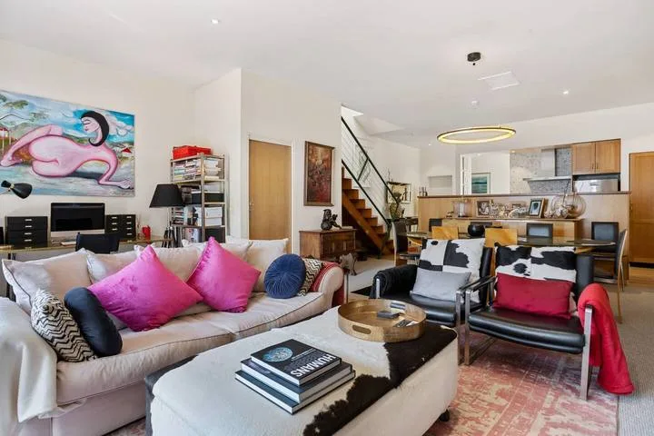 A living room with colorful seating, artwork, and an open kitchen beyond.
