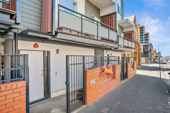 A modern apartment building with balconies and gated ground-floor entrances along the sidewalk.