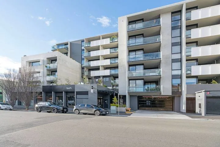 Modern apartment buildings line a street, with parked cars in front.