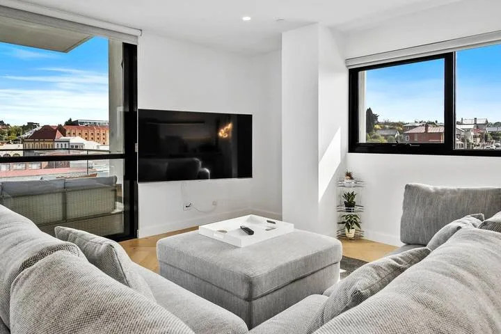 A bright living room with gray seating, a coffee table, and large windows.