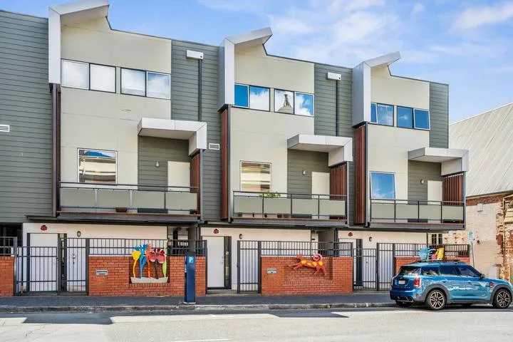 Modern multi-story residential buildings with balconies stand behind a brick-and-metal fence.