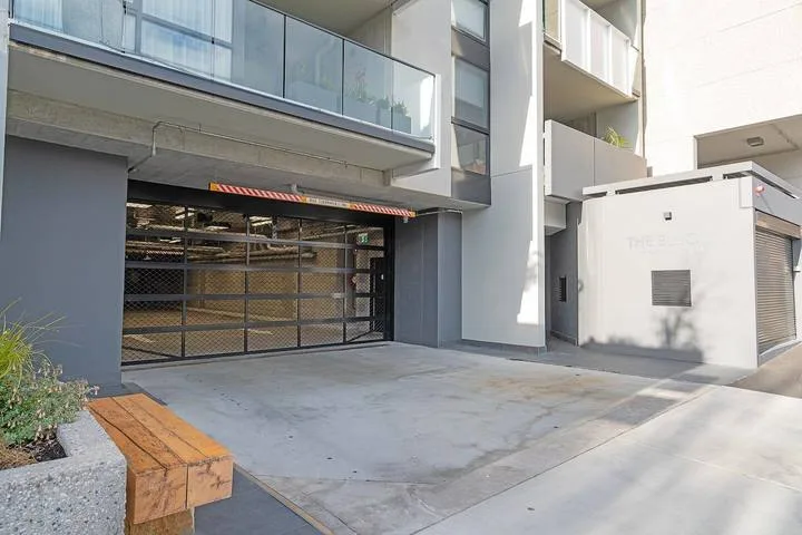 A modern building entrance opens onto a broad paved driveway.