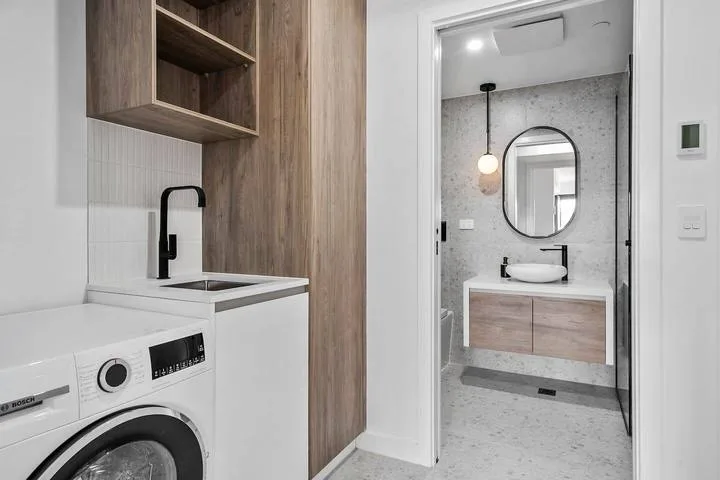 A laundry area with a washing machine and sink opens onto a bathroom with a vanity.