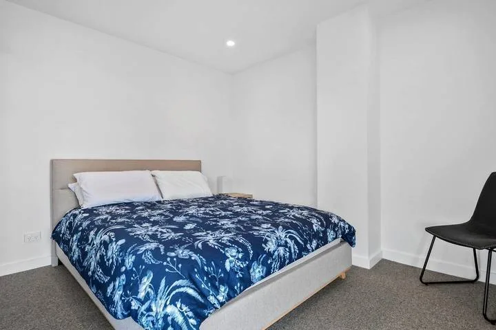 A bedroom with a bed covered in blue floral bedding and a black chair.
