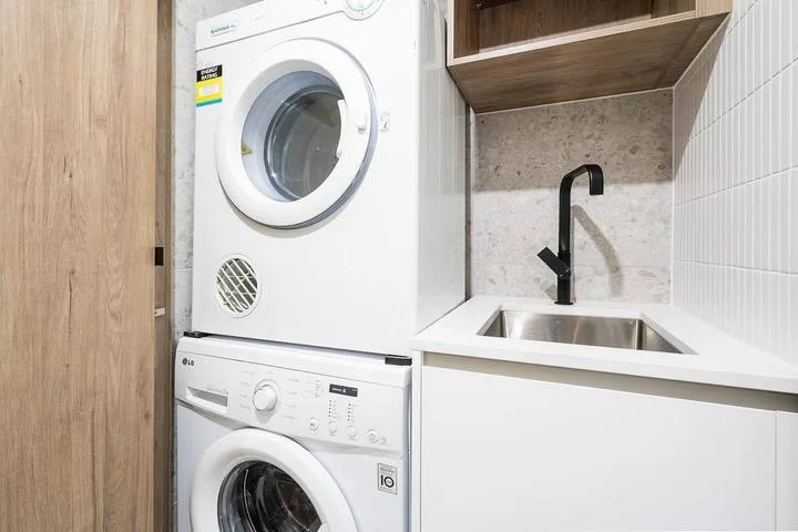 A laundry area with stacked appliances beside a sink and cabinetry.