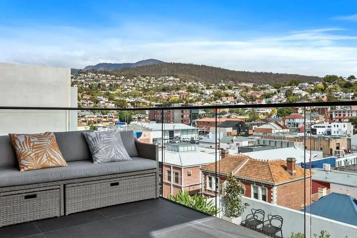 A balcony seating area overlooks a city with hills in the distance.