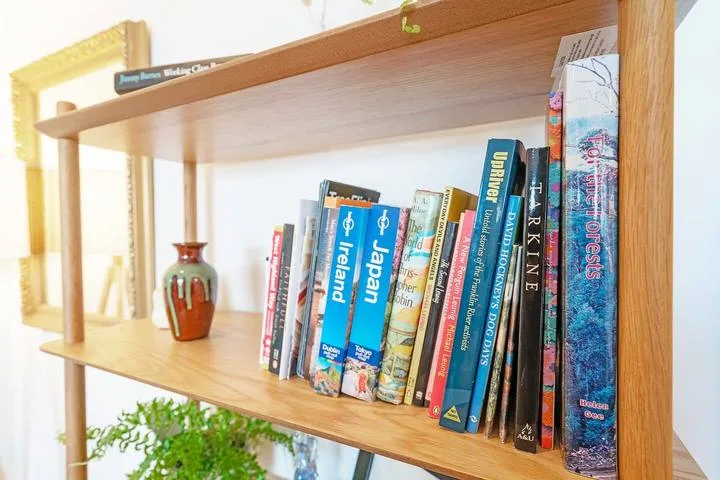 A wooden bookshelf displays travel books and a small decorative vase.