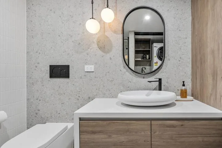 A modern bathroom vanity with a round basin, oval mirror, and hanging lights.