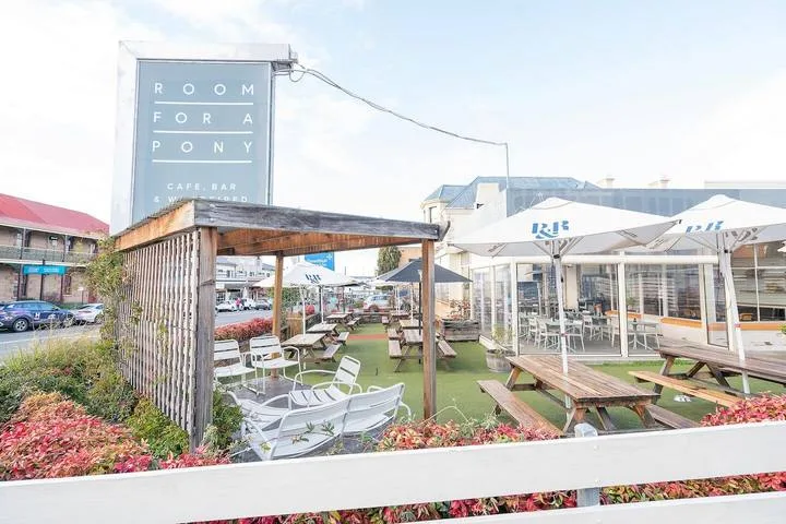 Outdoor café seating beneath a wooden pergola, with picnic tables and umbrellas.