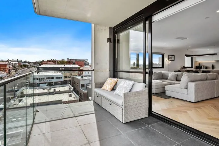 A balcony with wicker seating overlooks nearby city buildings.