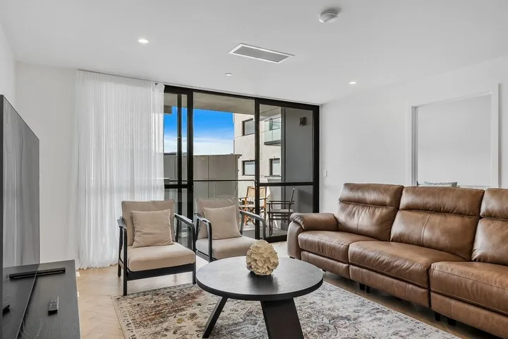 A bright living room with seating beside large glass doors opening onto a balcony.