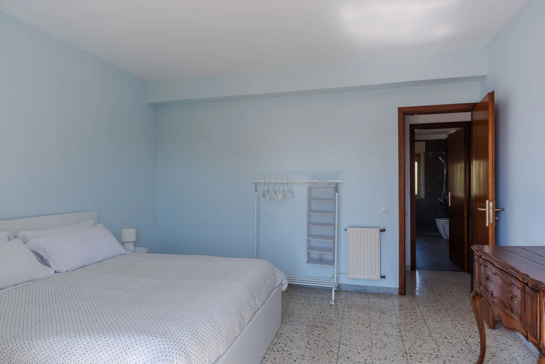 Un dormitorio con una cama, un perchero y una puerta abierta.