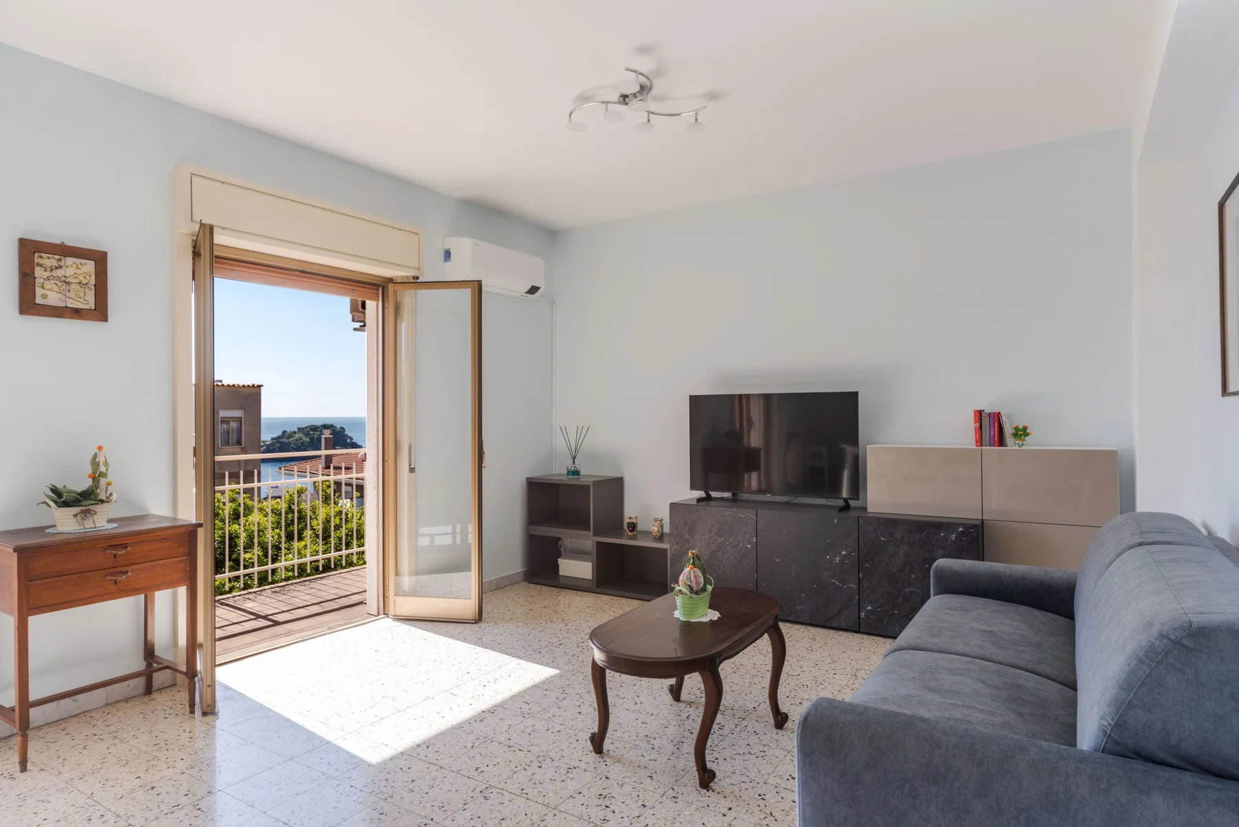 Una sala luminosa con televisor, asientos y una puerta abierta al balcón.