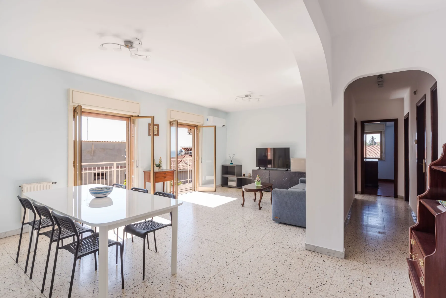 Una luminosa sala de estar y comedor con mesa, asientos y ventanas que dan a un balcón.