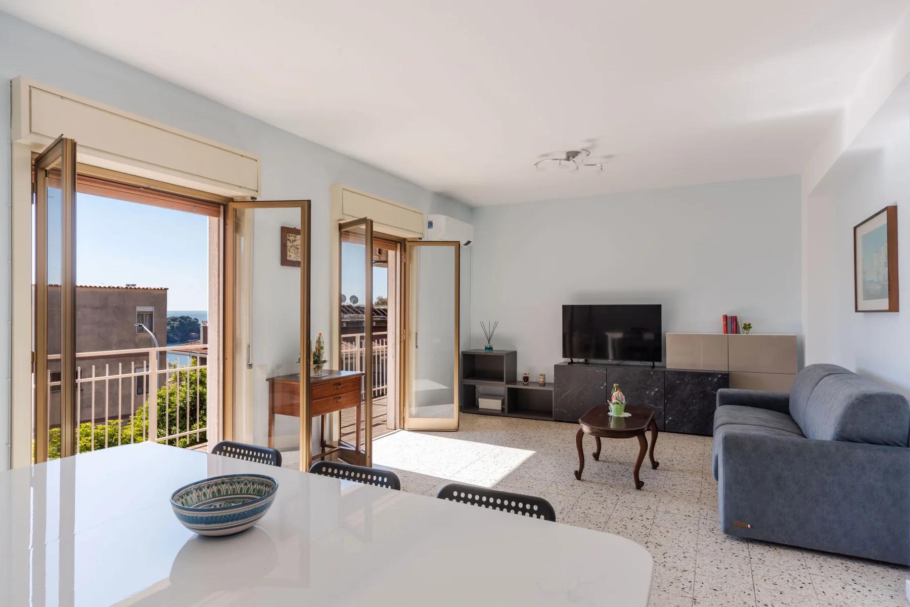 Una sala luminosa con televisor, asientos y puertas abiertas al balcón.