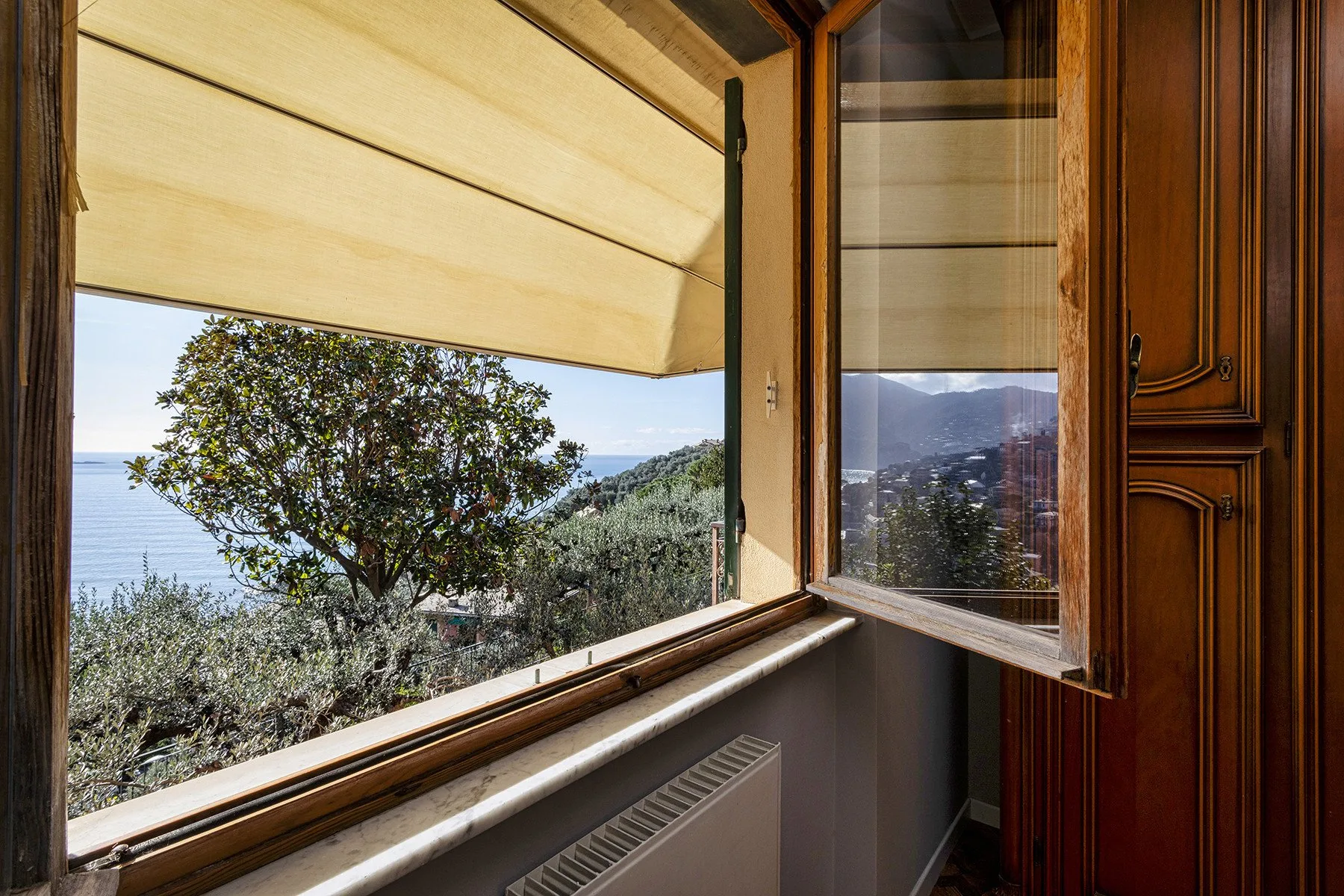 An open window overlooks a leafy hillside and the sea.