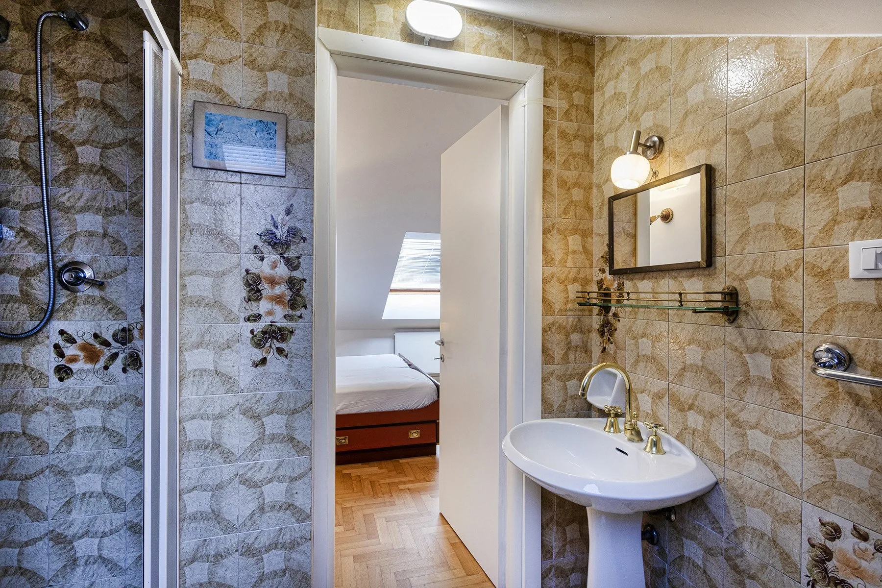A tiled bathroom with a pedestal sink and a shower beside an open doorway.