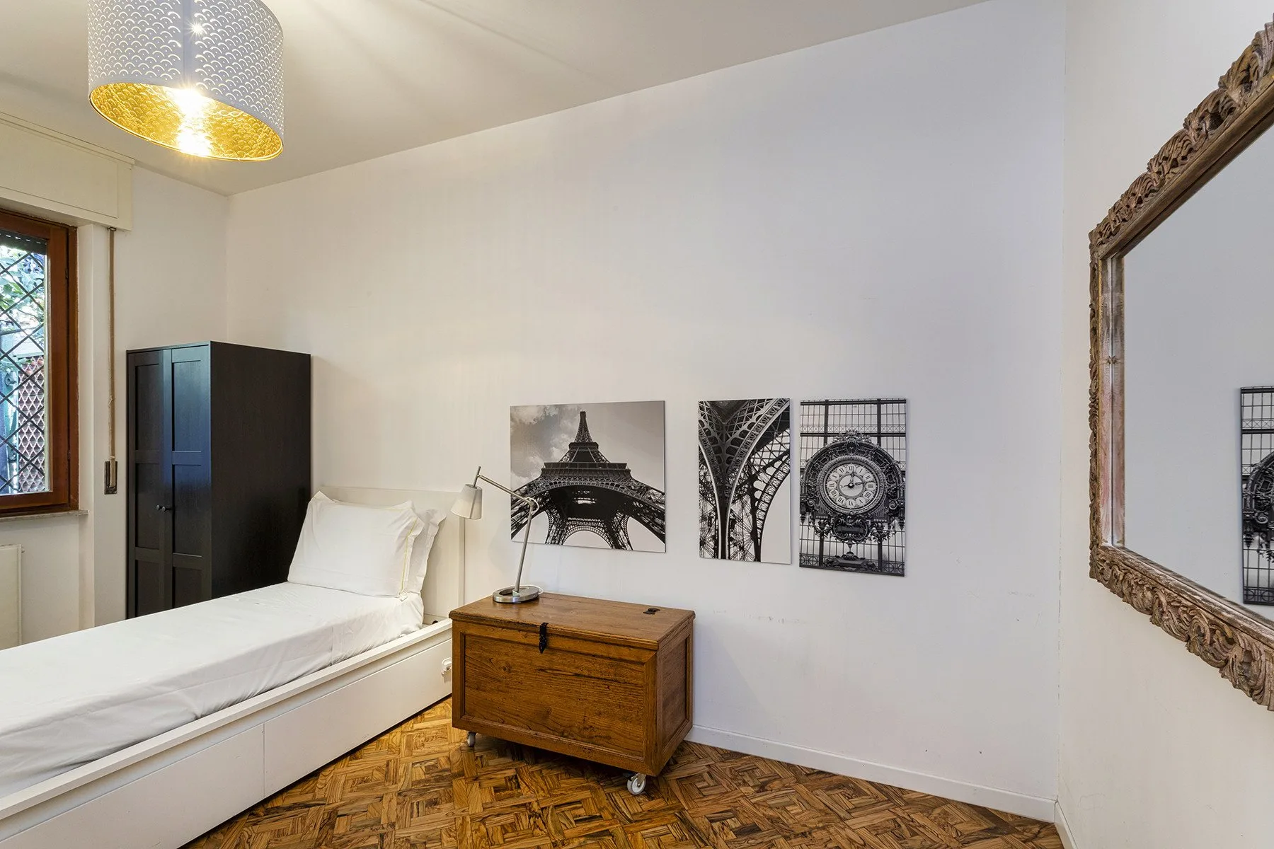 A bedroom with a single bed, wooden dresser, and black-and-white wall art.