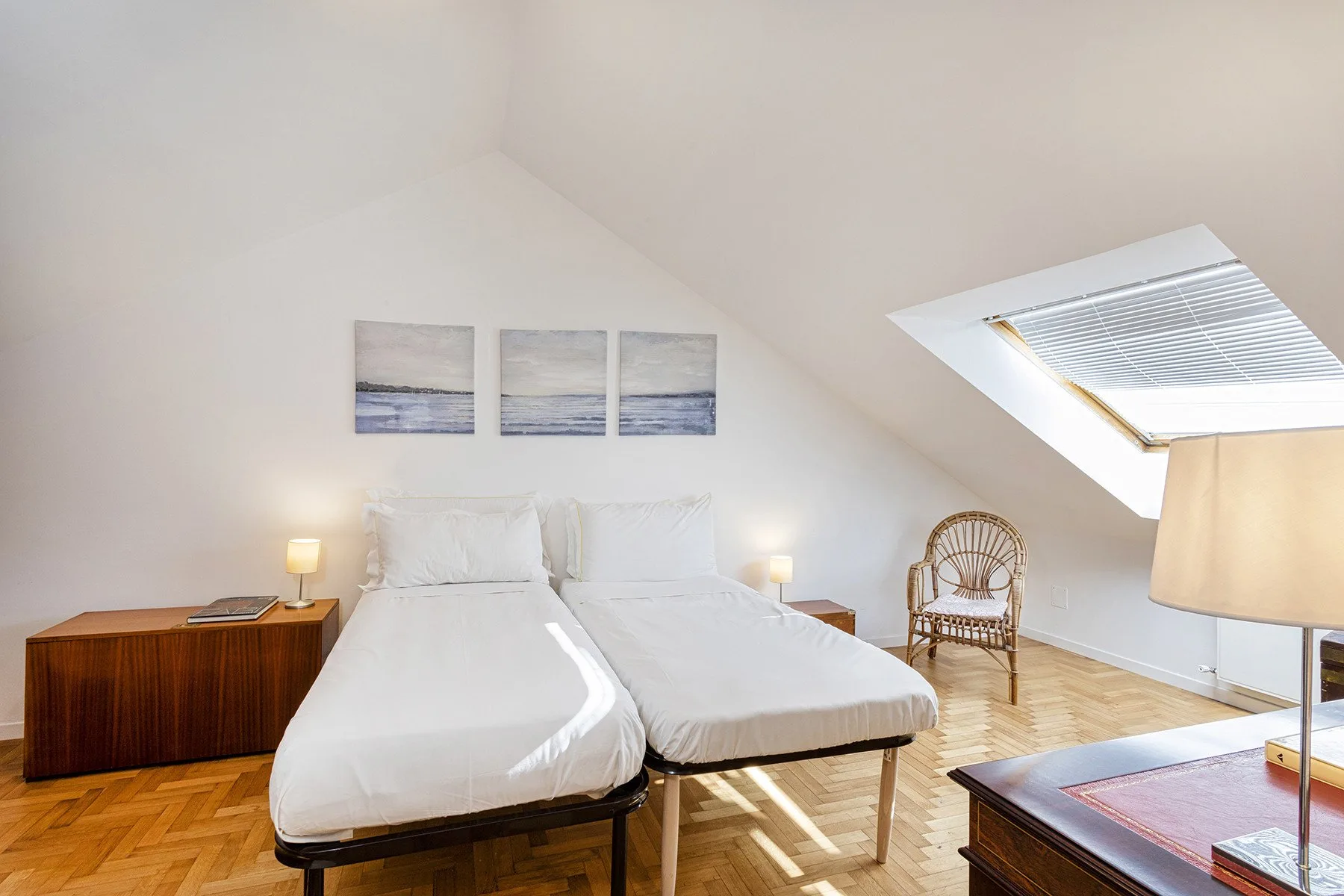 An attic bedroom with two beds, bedside tables, and a skylight.