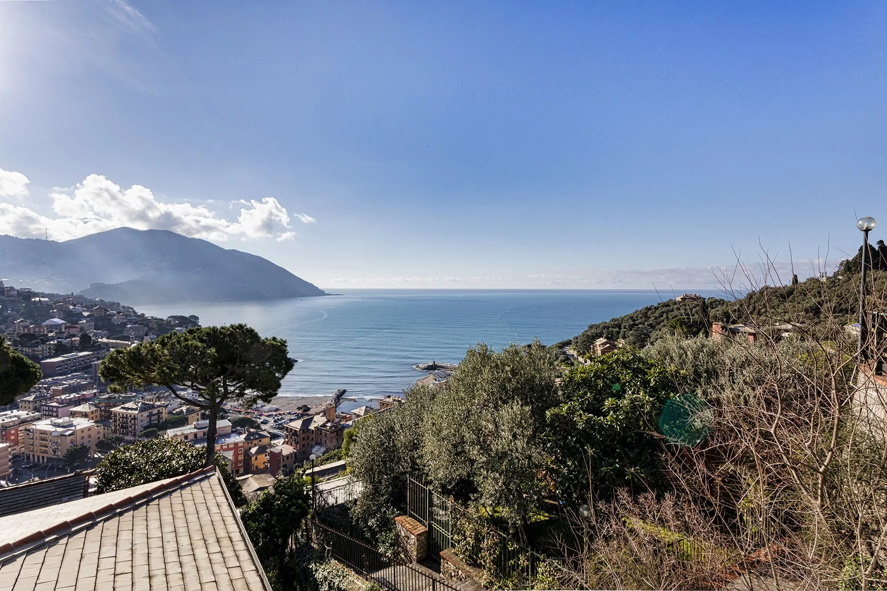 A coastal hillside overlooks a town and the sea beneath a clear sky.