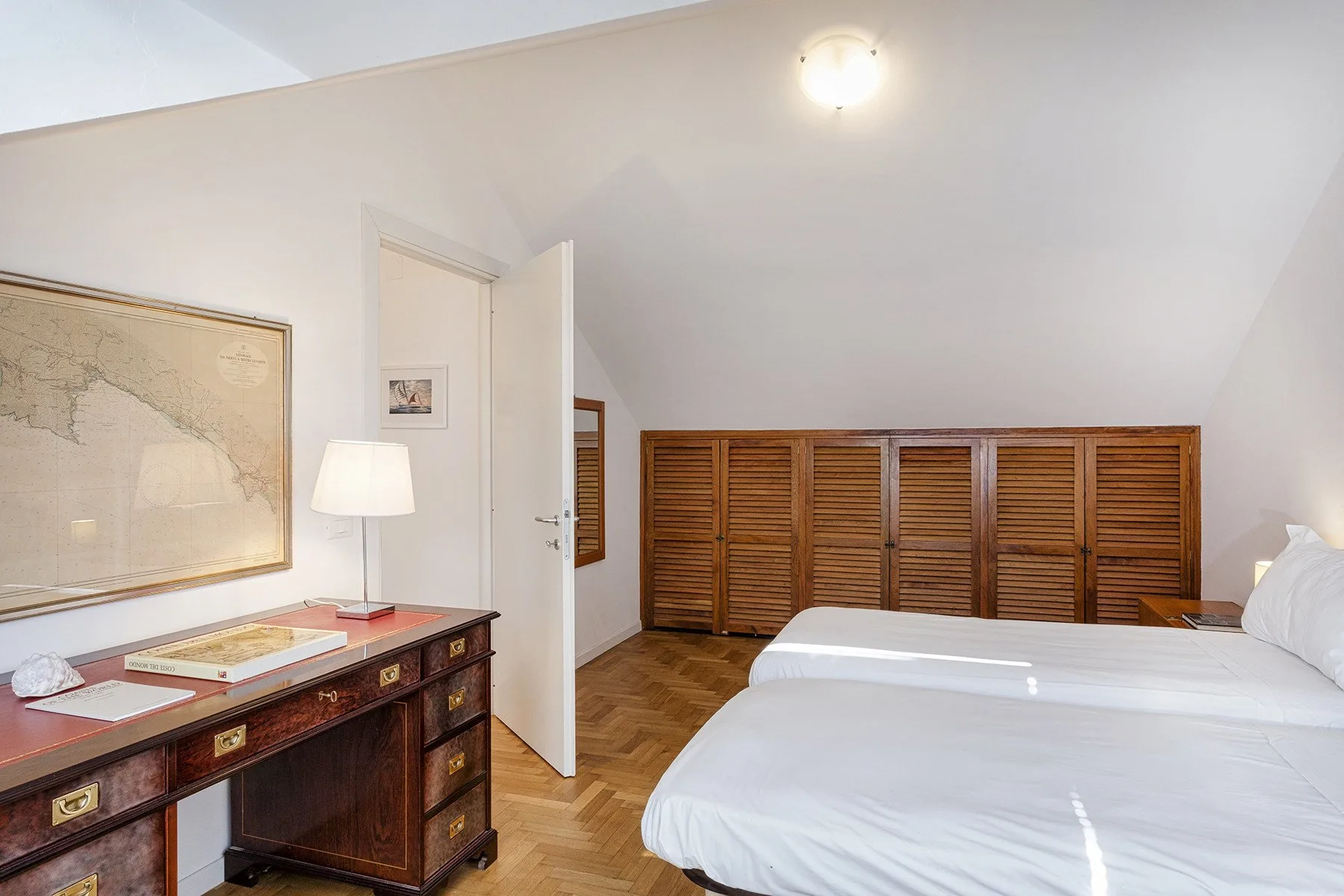 A bright bedroom with a bed, a wooden desk, and built-in cabinets along the wall.