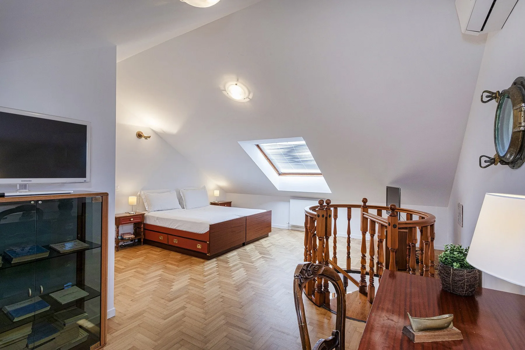 A furnished attic bedroom has a bed, a skylight, and a wooden railing.