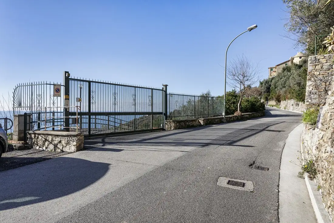 A paved road curves past a metal fence beside a stone wall.